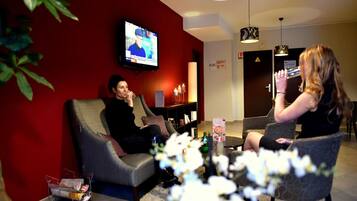 Una habitación con un televisor en la pared, una estantería y una zona de estar con dos sillones.