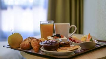 A breakfast tray with a pear, croissants, a glass of orange juice, a cup of coffee, and a bowl of fruit.