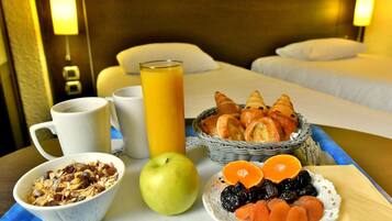Una mesa con un desayuno que incluye croissants, zumo de naranja, un bol de cereales, una manzana y un plato de fruta seca.