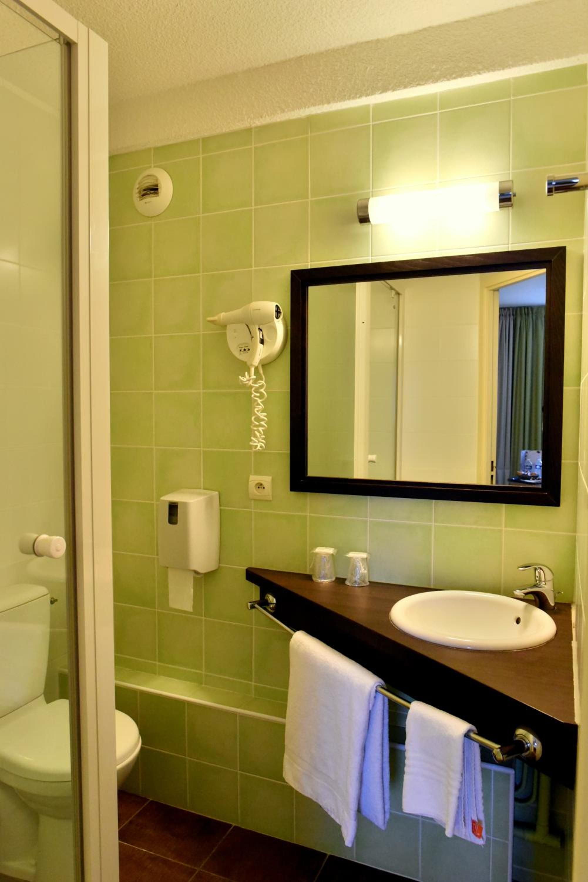 A bathroom with a green tiled wall, a white sink, a mirror, a hairdryer, and a towel rack.