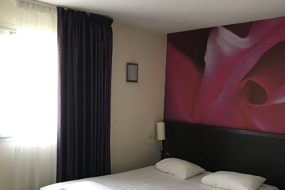 A neatly made bed with white linens and pillows, a dark headboard, and a large abstract painting on the wall.