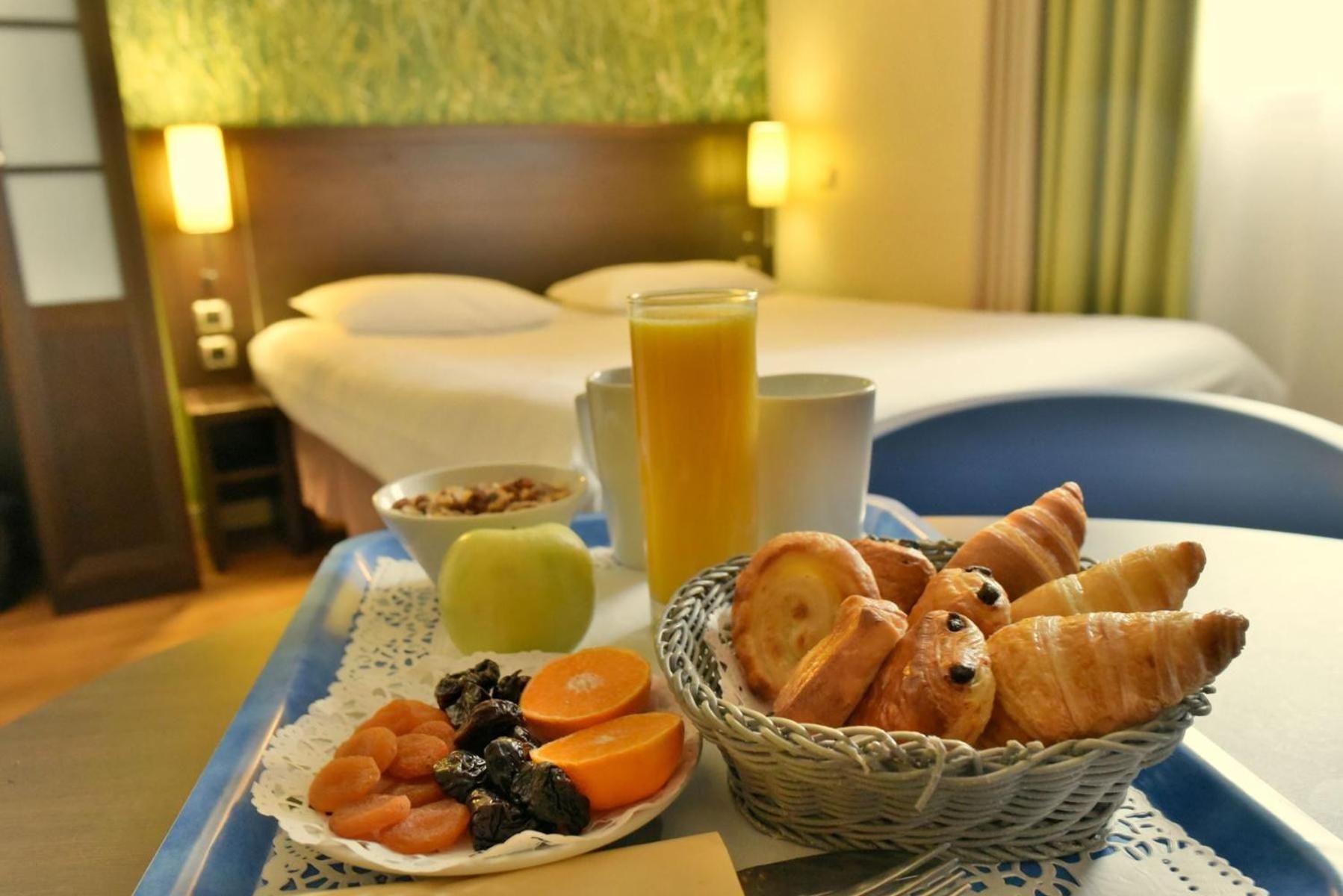 Un plateau de petit-déjeuner avec des viennoiseries, des fruits et un verre de jus d’orange, posé sur une table dans une chambre d’hôtel.