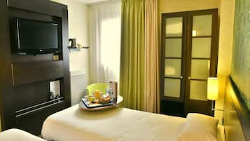 A hotel room with two beds, a television, a tray with breakfast items, and a lamp.