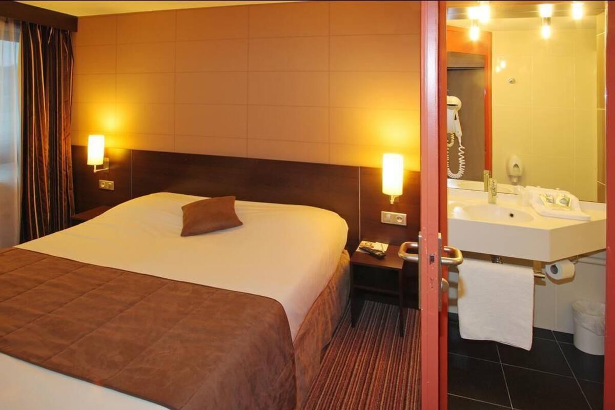 A hotel room with a large bed, bedside lamps, a nightstand, a bathroom with a sink, mirror, and towel rack.