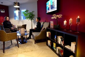 A reception area with a television, seating, a bookshelf, and a plant. - Hotel Inn Design Chambery - La Ravoire (La Ravoire)