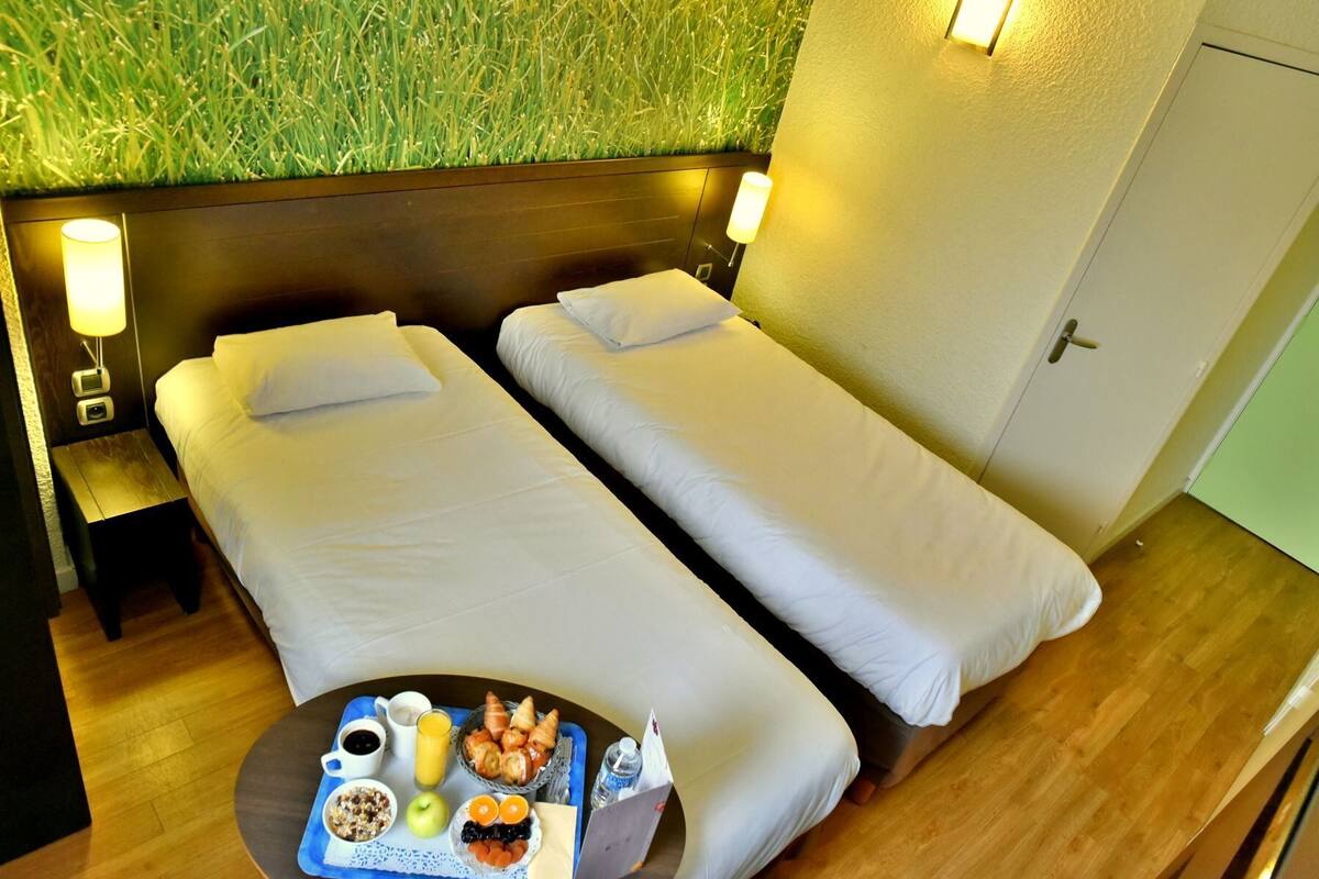 A hotel room with two single beds, a small table with breakfast, and a green wall.