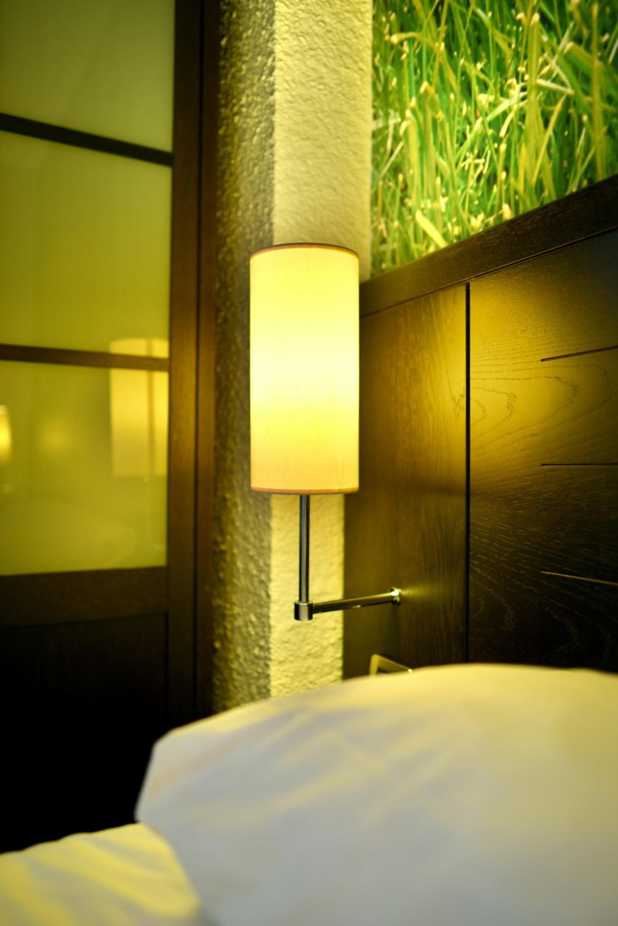 Una habitación de hotel con cama, lámpara de pared y pared con textura.