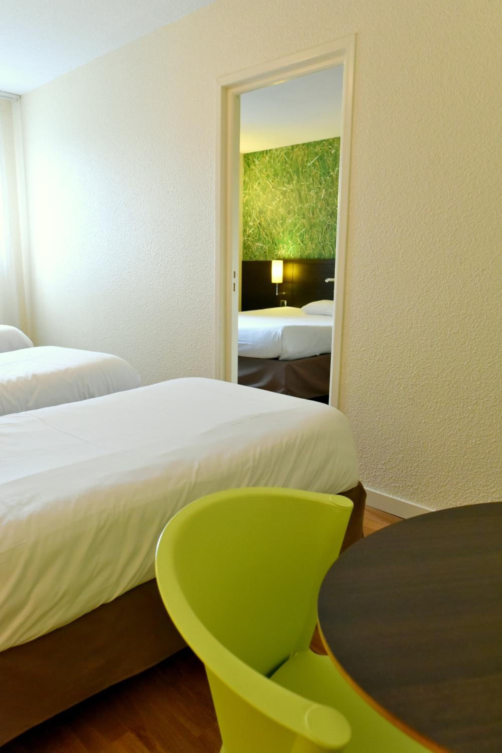Une chambre d’hôtel avec deux lits, un fauteuil vert et une petite table.