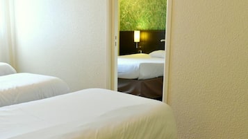 Une chambre d’hôtel avec deux lits, un fauteuil vert et une petite table.