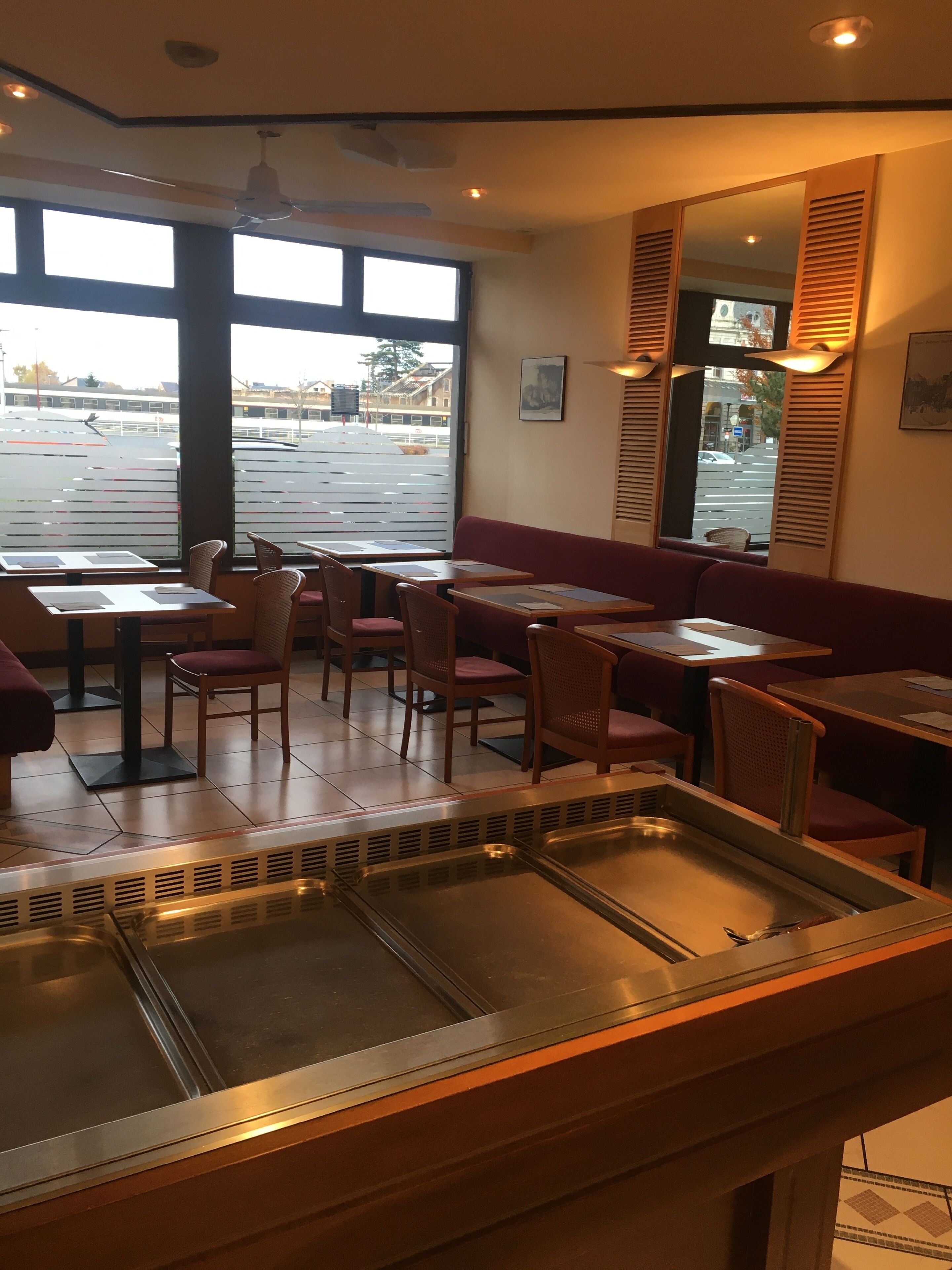 En restaurantindretning med borde, stole, et buffetområde og store vinduer.