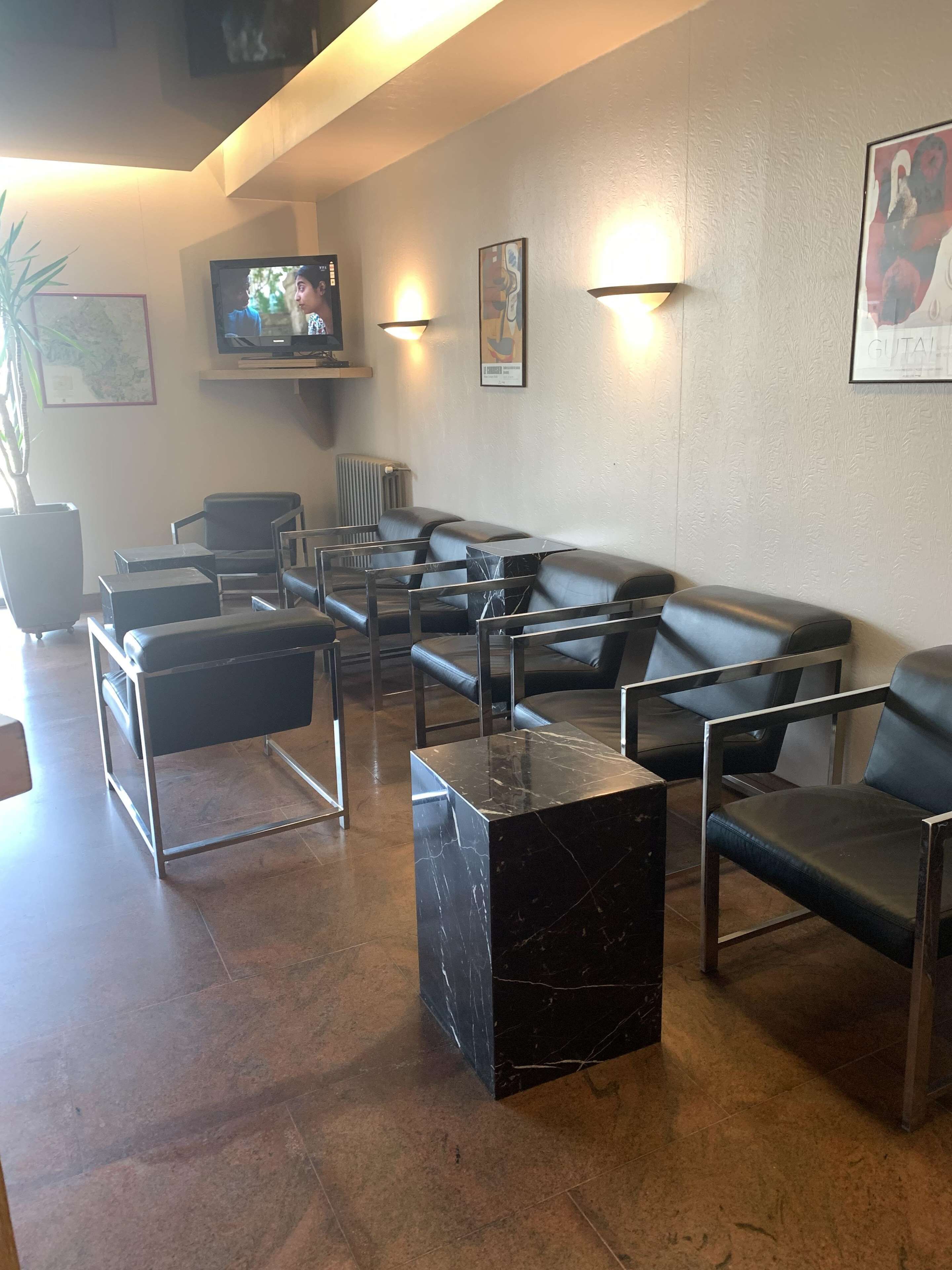 Ein Wartebereich mit Ledersitzgelegenheiten, einem Marmortisch und einem Fernseher an der Wand.