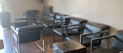 Un área de espera con asientos de cuero, una mesa de centro de mármol y un televisor en la pared.