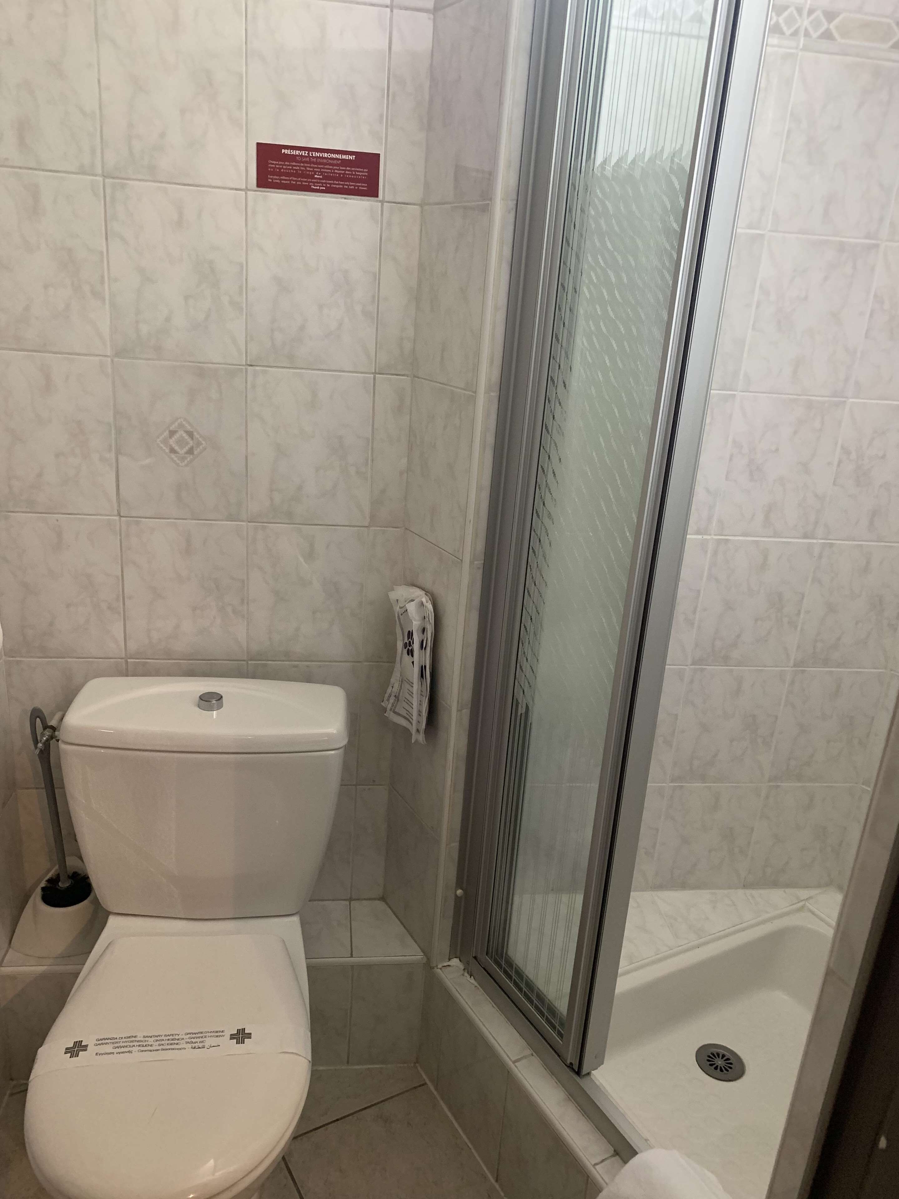 A bathroom with a toilet, a shower with a glass door, and a sign on the wall.