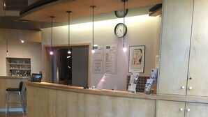 A reception area with a wooden counter, a clock, and a menu board. - Hotel Kyriad Rodez (Rodez)