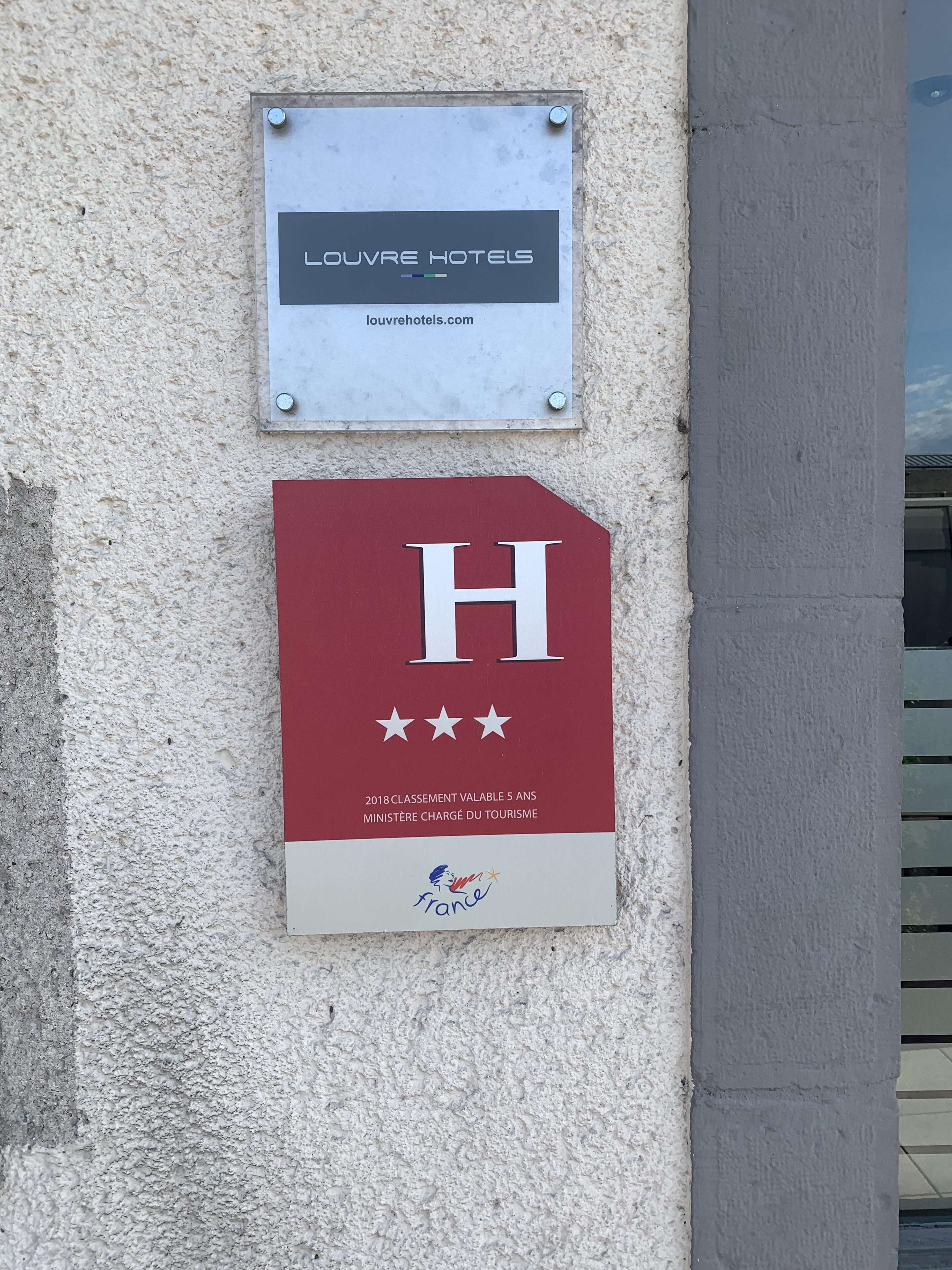 Et hotelskilt med navnet "LOUVRE HOTELS" og en hjemmesideadresse. Under skiltet er der et rødt skilt med et hvidt 'H' og tre stjerner, der angiver en 5-stjernet vurdering.