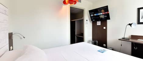A hotel room with a bed, a TV mounted on the wall, a desk with a chair, and a door leading to a closet.