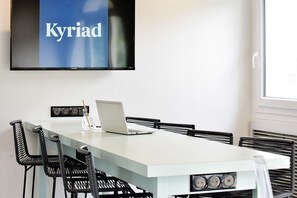 A conference room with a long table, four chairs, a laptop, and a TV displaying 'Kyriad'. - Hôtel Kyriad La Rochelle Centre Ville (La Rochelle)