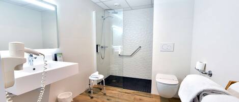 A modern bathroom with a white sink, a hairdryer, a glass shower enclosure, a toilet, and a wooden floor.
