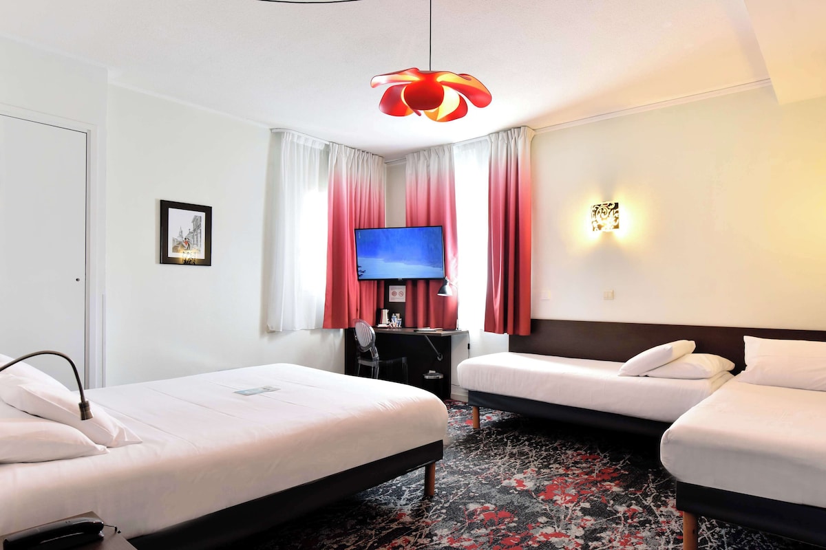 A hotel room with two beds, a desk with a computer, a TV, and a red pendant light.