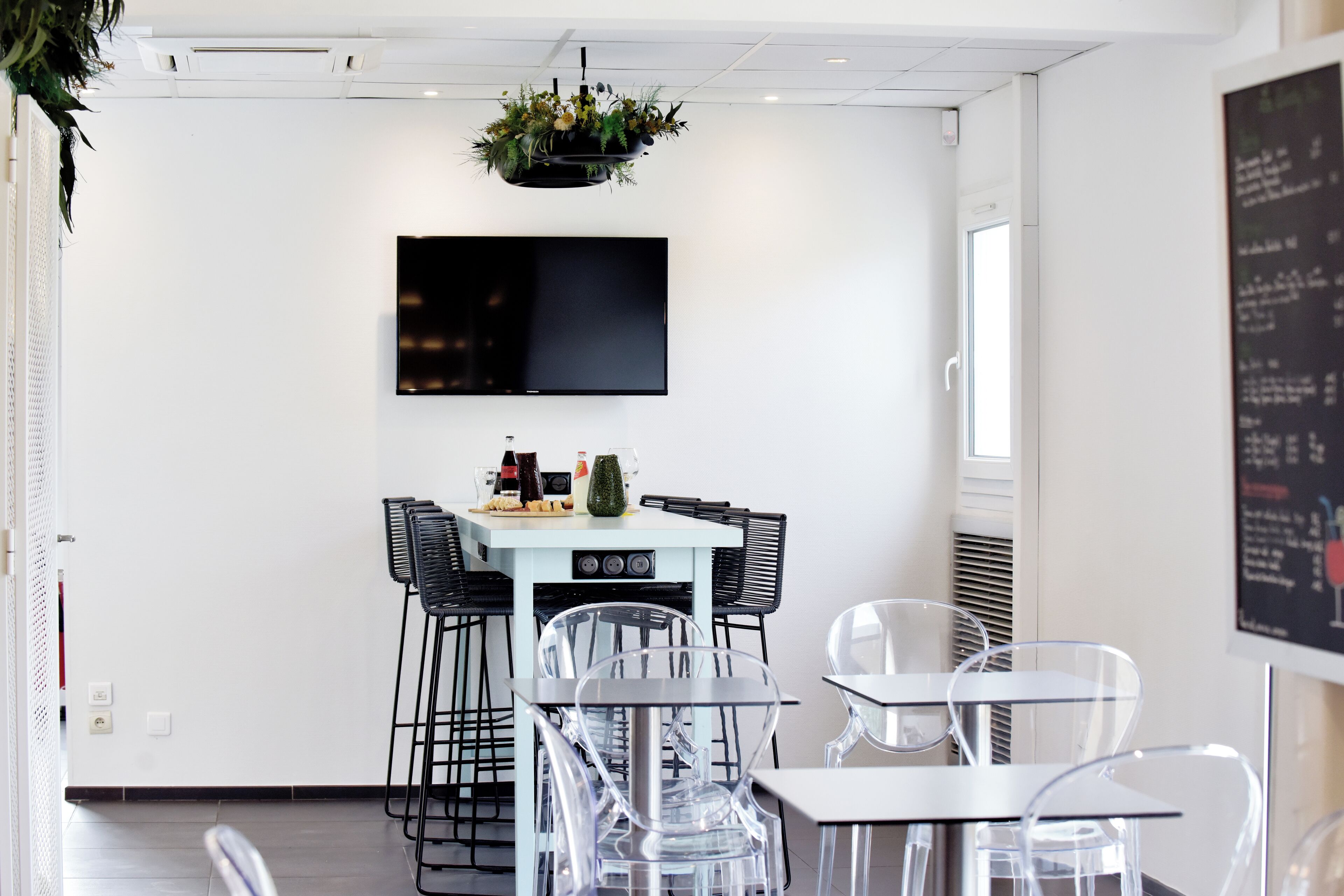 Un comedor moderno con una mesa blanca, sillas negras y un televisor montado.
