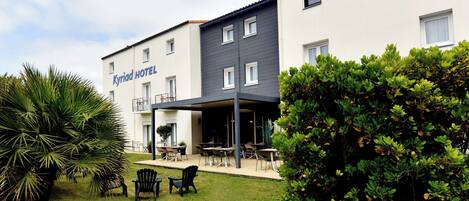 A hotel with a covered outdoor seating area, a well-maintained lawn, and a variety of seating options.