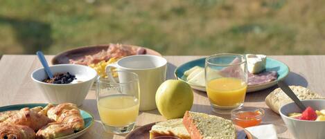 Une table de petit-déjeuner avec des croissants, du pain, des fruits et des boissons.