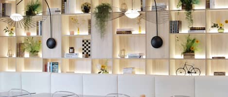 Un interior moderno con asientos acolchados blancos, mesas de vidrio transparente y estanterías con libros y plantas.