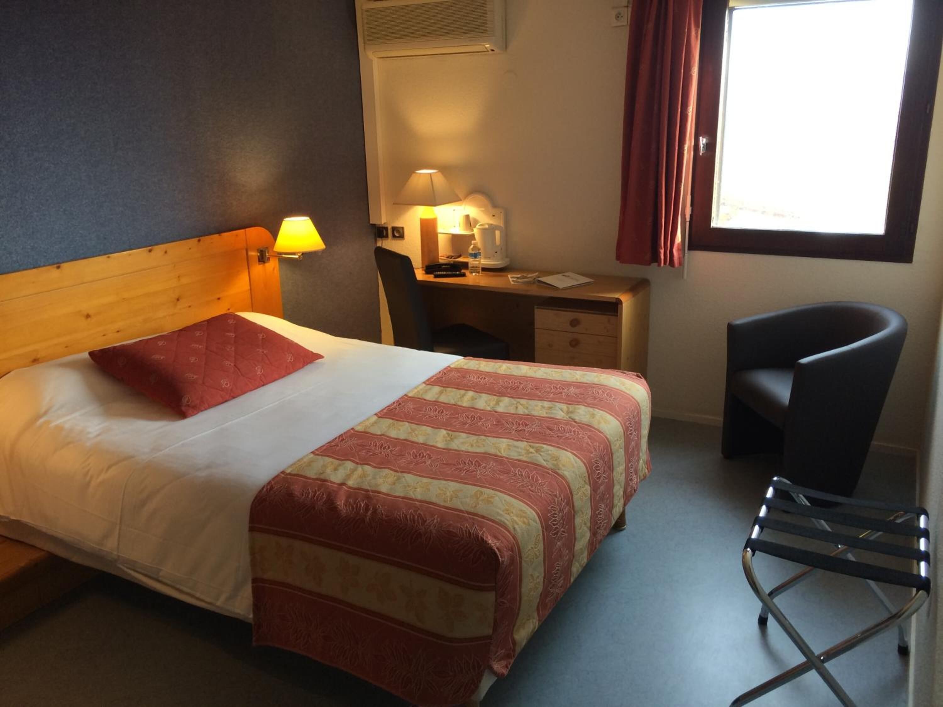 Een hotelkamer met een bed, bureau, stoel en raam.