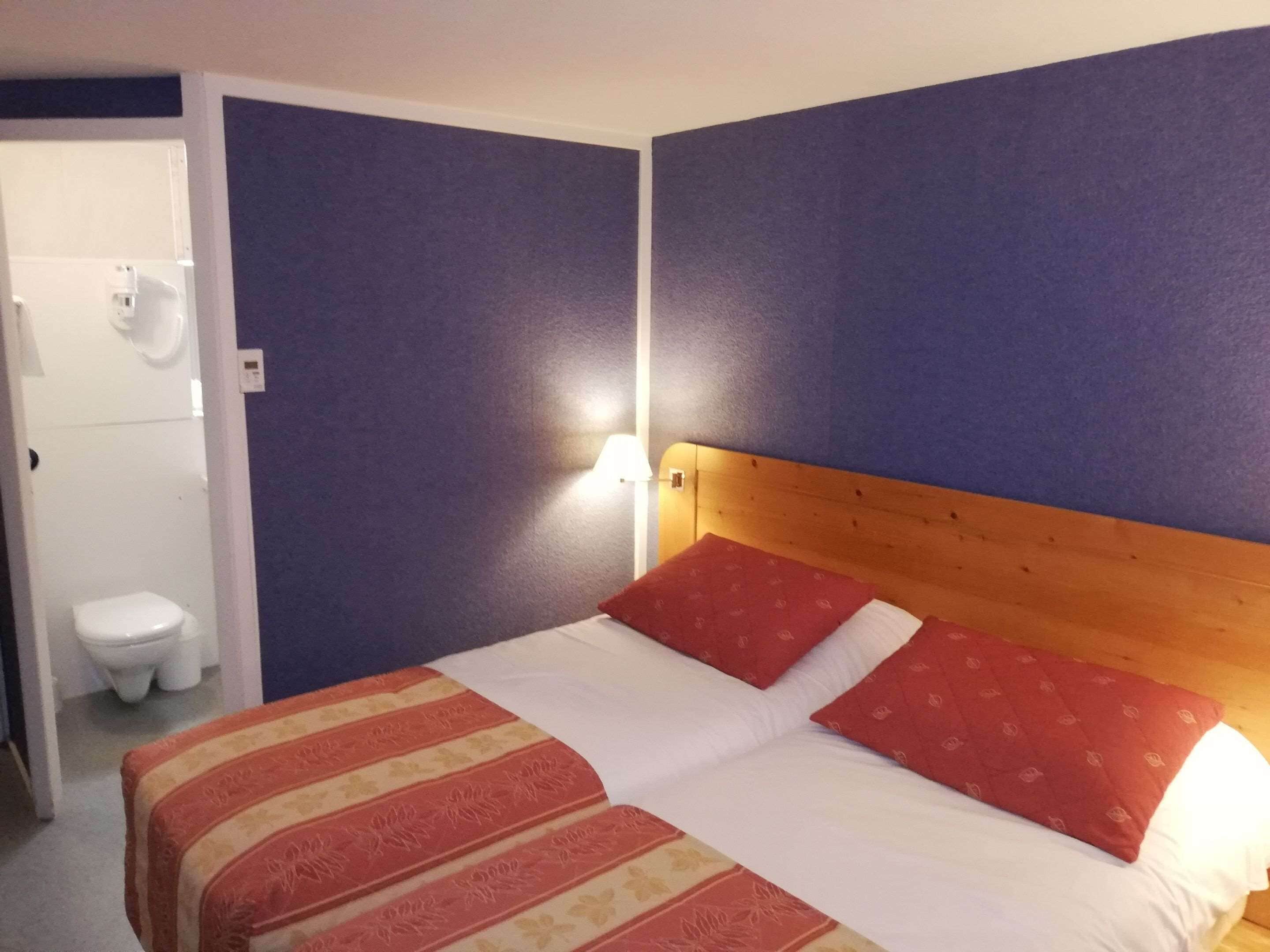 A hotel room with a bed, a wooden headboard, and a wall-mounted nightlight.