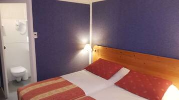 A hotel room with a bed, a wooden headboard, and a wall-mounted nightlight.