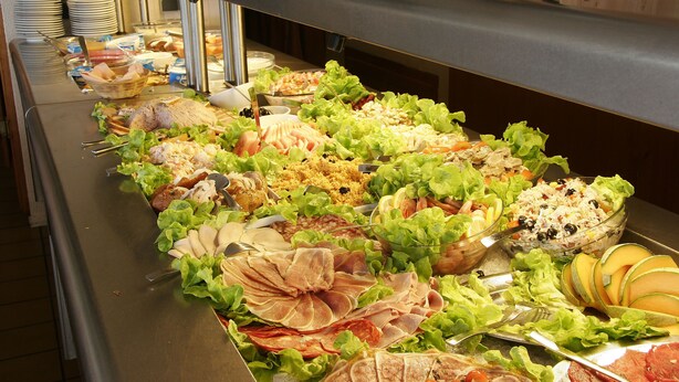 Buffet com diversos alimentos, incluindo saladas, carnes e frutas.