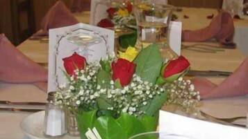 Ein gedeckter Tisch mit einer Mittelstückanordnung aus roten und gelben Rosen, weißen Blüten und einer Glasvase.