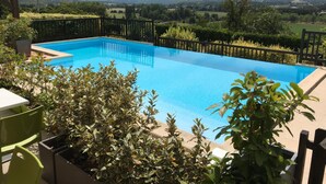 Piscina retangular com cerca de metal preta, rodeada por vegetação e vista para uma paisagem montanhosa.
