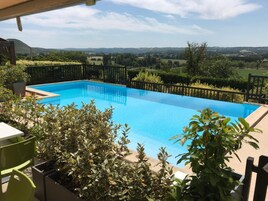 Piscina retangular com cerca de metal preta, rodeada por vegetação e vista para uma paisagem montanhosa.