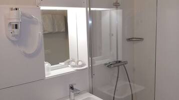 Un baño moderno con ducha envuelta en vidrio, lavamanos blanco y un secador de pelo fijado en la pared.