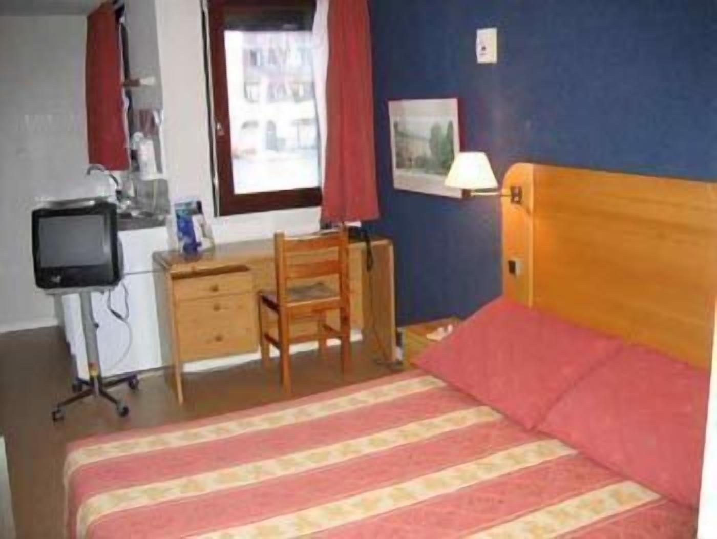 Een slaapkamer met een bed, een bureau, een stoel, een televisie en een raam.