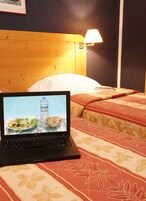 Um laptop sobre a cama, que tem cabeceira de madeira, uma luminária e um edredom estampado.