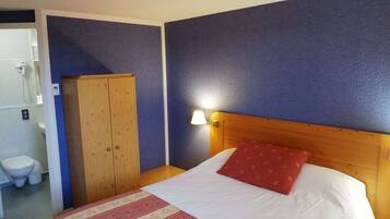 Une chambre à coucher avec une tête de lit en bois, un lit recouvert d’une couvre-lit à motifs floraux, un oreiller rouge et une table de chevet avec une lampe.