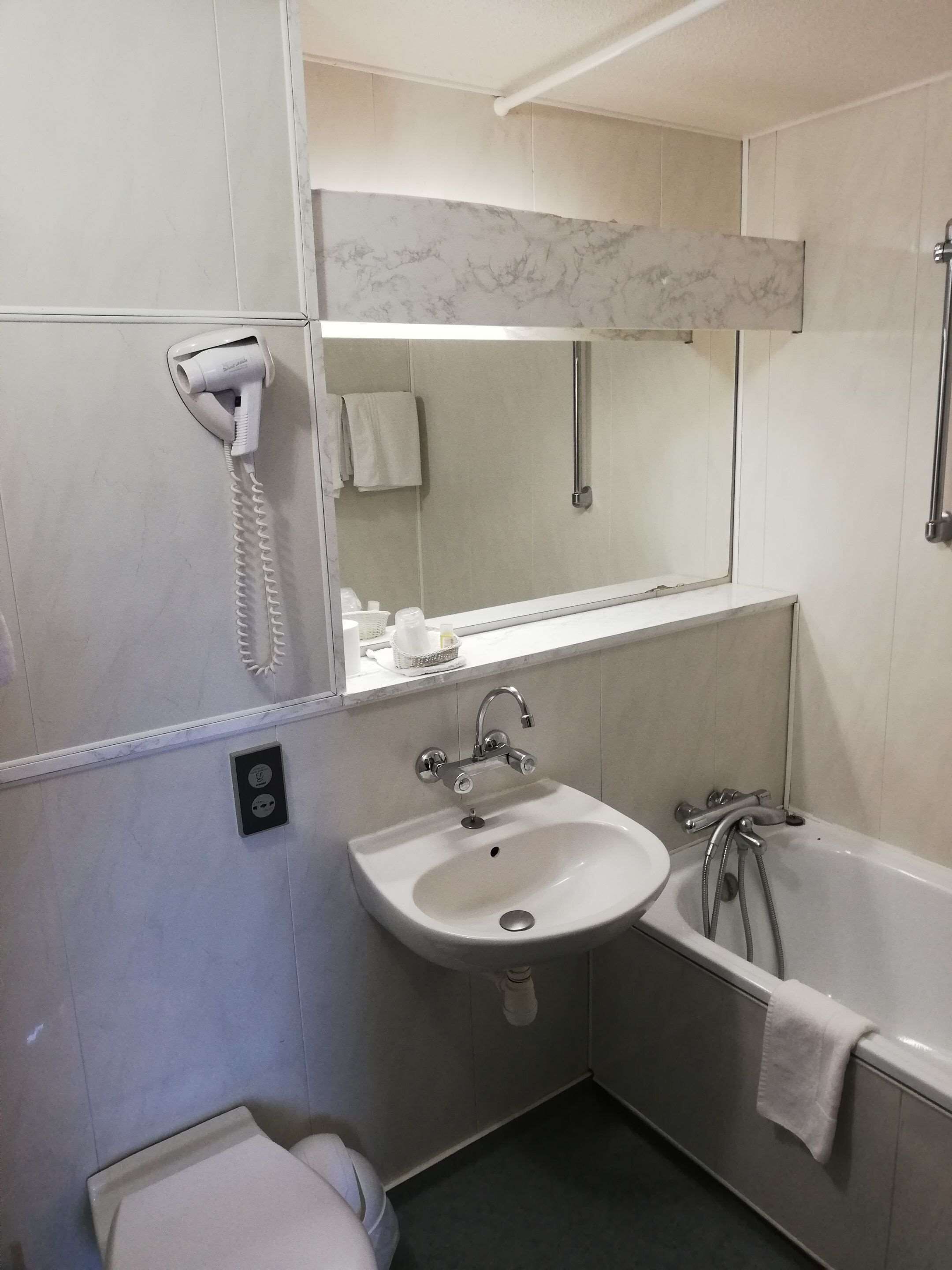 A bathroom with a white sink, a mirror, a hairdryer, a bathtub, and a toilet.