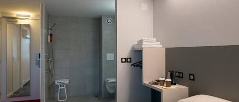 Habitación de hotel con cama, mesita de noche con cafetera, zona de ducha y retrete.