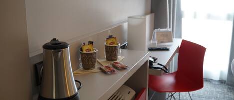 Habitación de hotel con kitchenette equipada con cafetera, tostadora y un refrigerador pequeño. Se observa una silla roja y un televisor de pantalla plana montado en la pared.