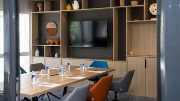 Un salón de conferencias con una televisión de pantalla plana grande, mesas de madera y sillas.