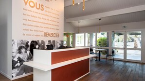 A hotel reception area with a modern design, featuring a reception desk, a large welcome sign, and a view of the outdoors through large windows.