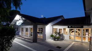 A hotel with a reception area, a well-lit entrance, and potted plants outside.