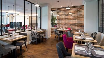 A modern restaurant with wooden tables and chairs, brick walls, and large windows.