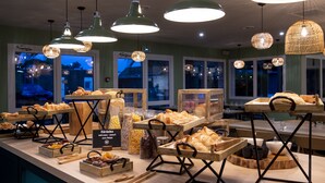 A breakfast buffet with various pastries and beverages, wooden serving boards, and hanging wicker lamps.