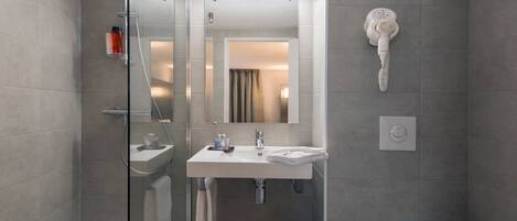A modern bathroom with a glass shower enclosure, a white sink, a toilet, and a hairdryer mounted on the wall.
