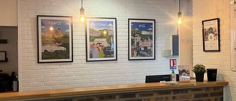 Un espace d’accueil avec un comptoir en briques, trois affiches encadrées accrochées au mur et des lampes suspendues.