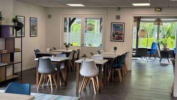 A modern dining area with tables and chairs, large windows, and indoor plants.