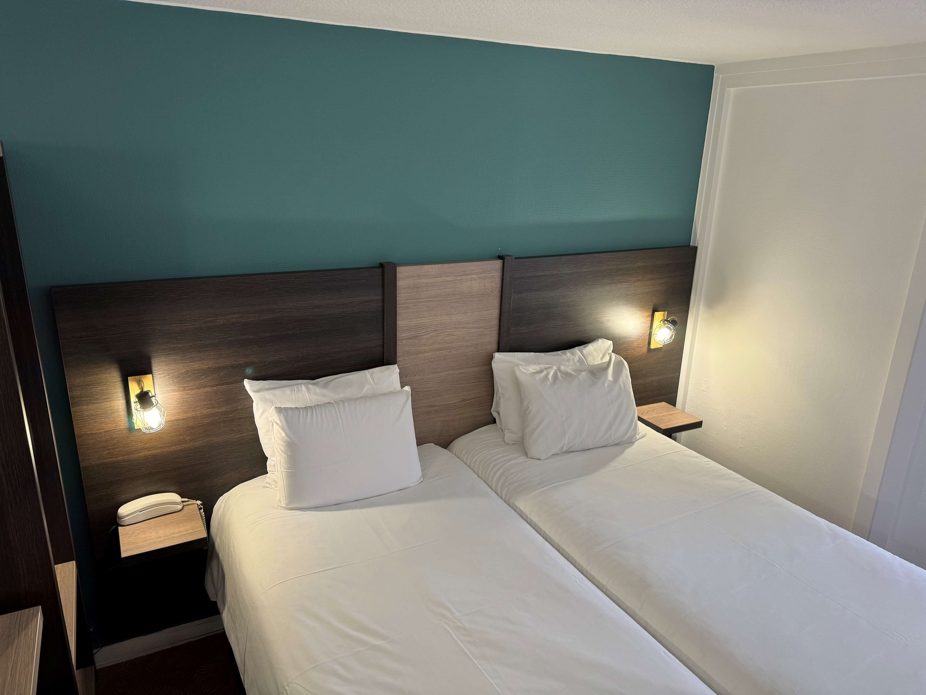 A double bed with white linens, two bedside tables with lamps, and a telephone on the left table.